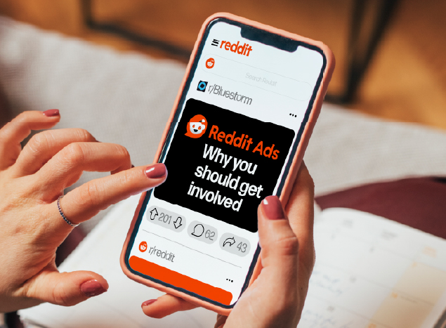Close-up of a phone being held, showing the Reddit platform with a post titled 'Reddit Ads: Why you should get involved'.